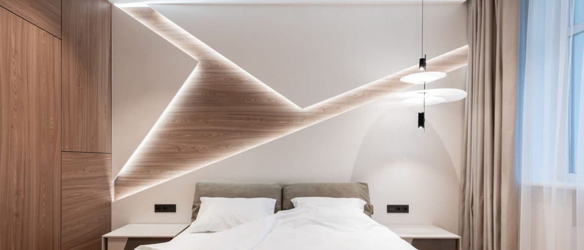 Modern bedroom with wooden walls and a large bed at the centre with lights integrated in wall feature