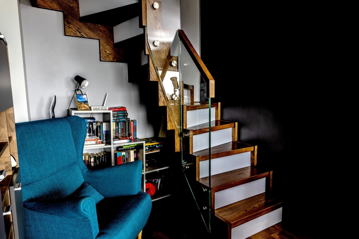 A corner under the stairs with a bookshelf and a comfortable blue chair
