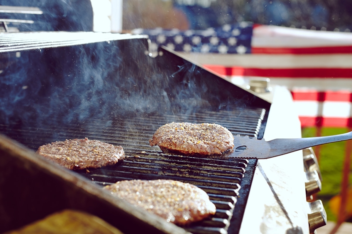 Burgers and hotdogs cooking over flames on grill for a 4th of July party