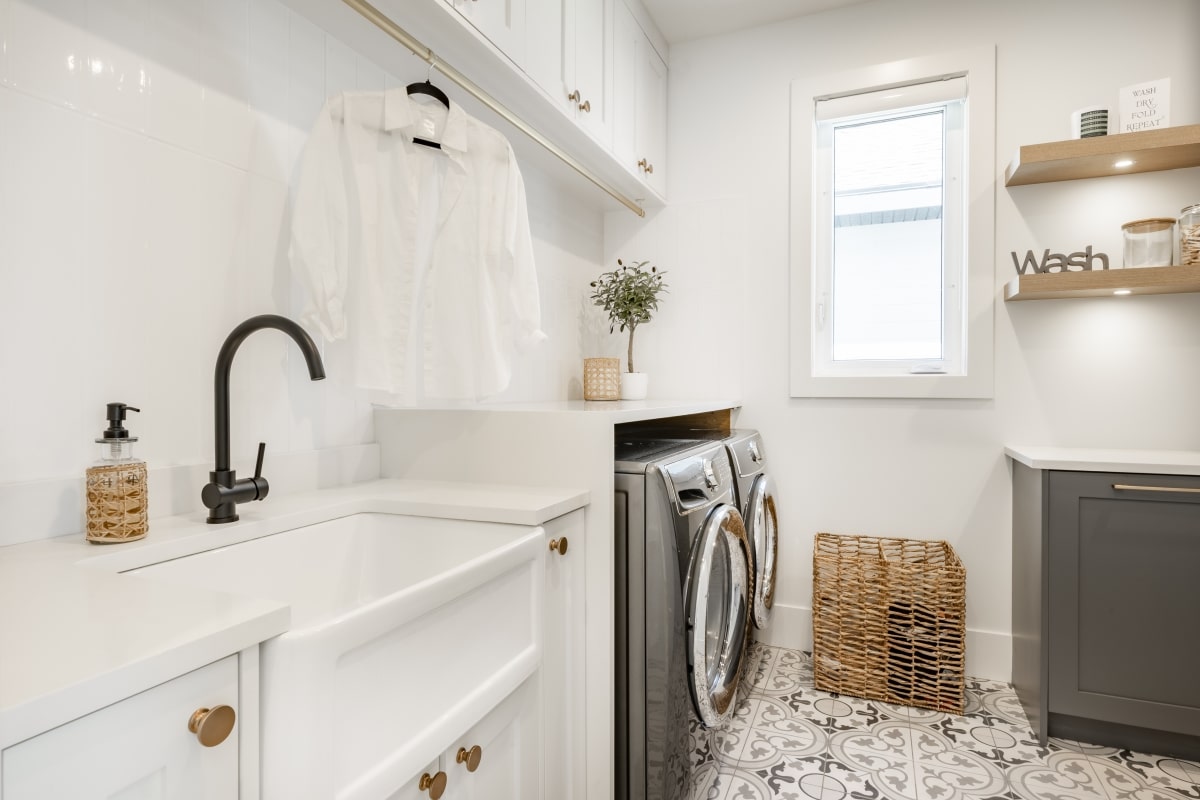 large laundry room with tiled floor dark washer and dryer white cabinets and a wicker basket below floating wooden shelves