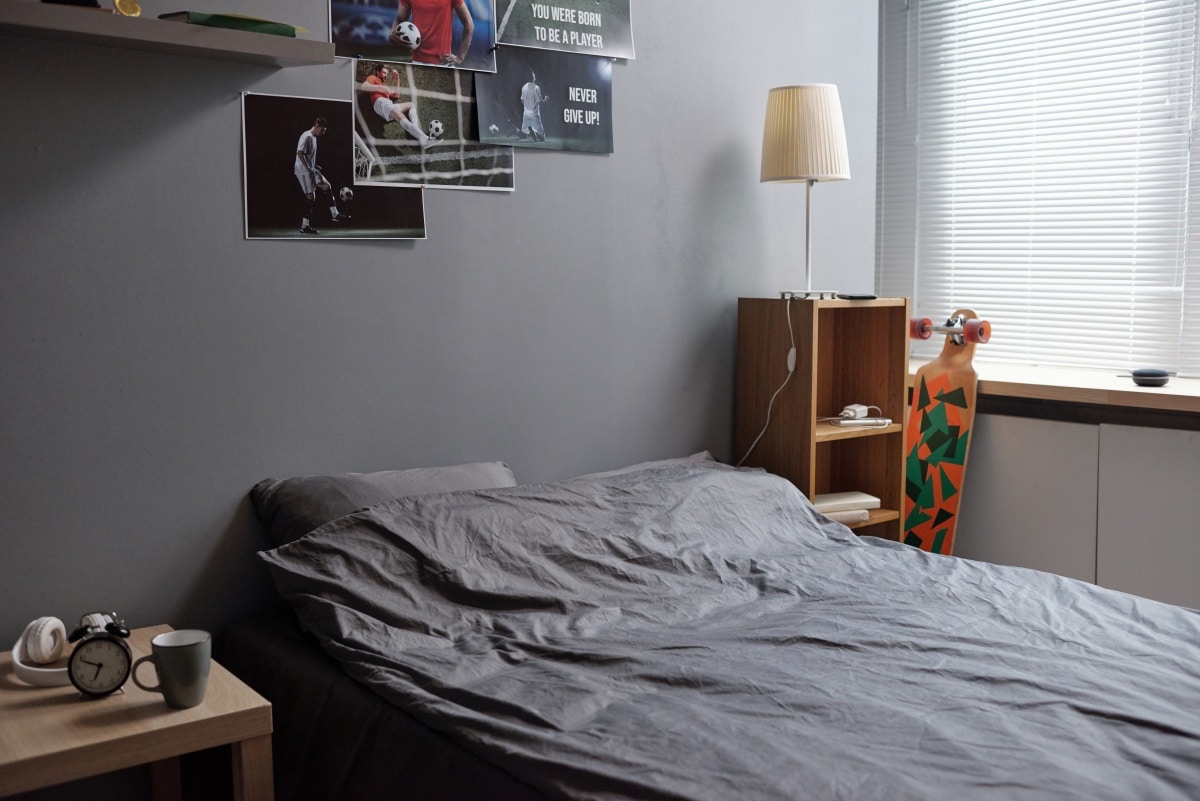 Double bed with grey pillows and sheets standing by wall with posters of football players in bedroom
