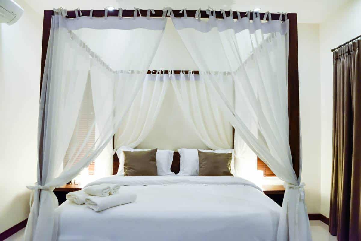 bedroom with wooden four poster bed with white bed linen and sheer curtains