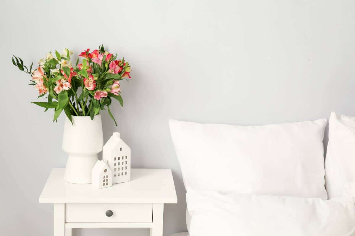 Vase with beautiful alstroemeria flowers and decor on bedside table in bedroom