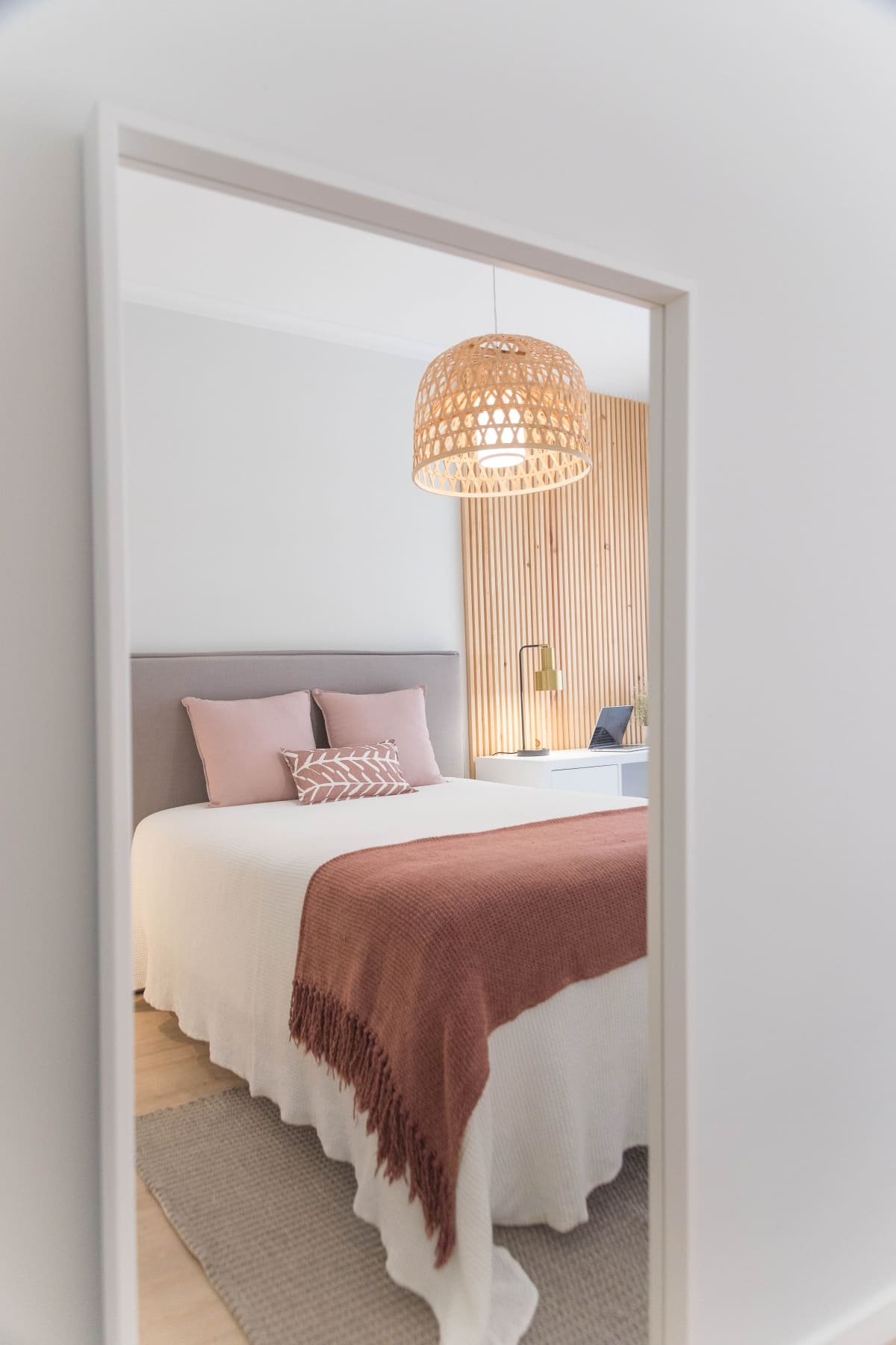 White bed with pinkish sheets and a rattan pendant light