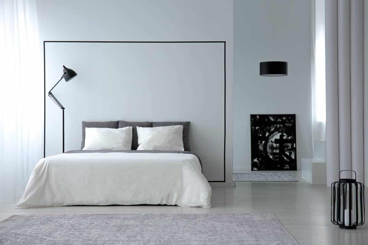Interior of white minimalistic bedroom with king-size bed, lamps and painting