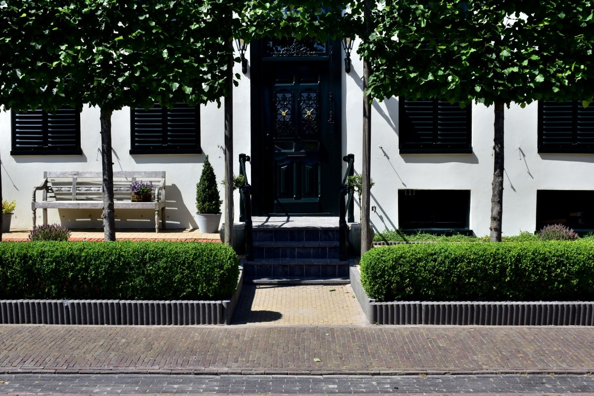 Facade of a house framed by trees and manicured hedges