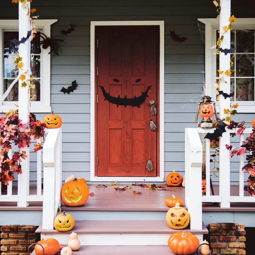 A front door decorated with pumpkins, cobwebs, and paper bats for Halloween.