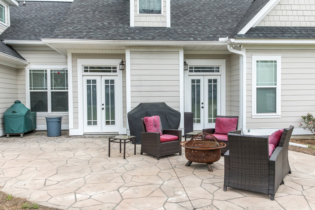 The back rear view of a home with a covered up barbecue and patio furniture with a stamped concrete patio floor