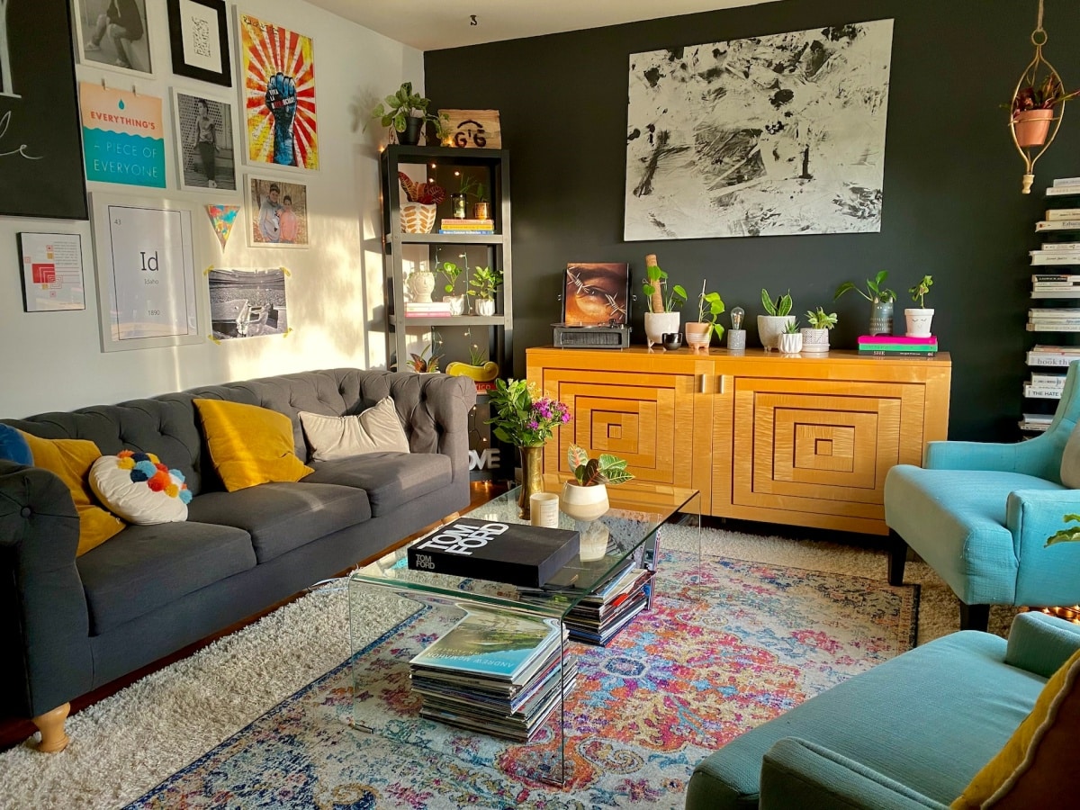 Cluttered living room with a black sofa, wooden cabinet, and black feature wall with paintings