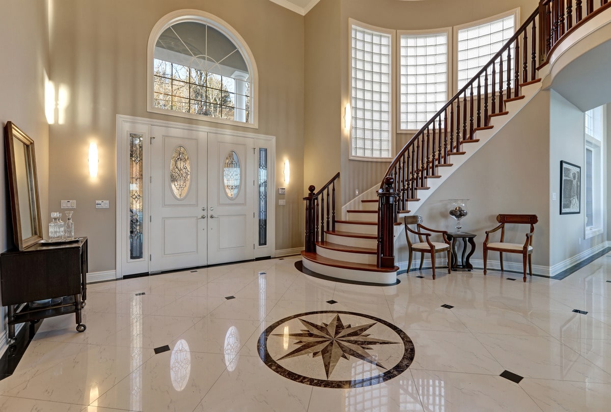 two story entry foyer with lots of space, marble mosaic tile floor, front door framed with arch window and sidelights, and grand staircase with glossy wood curved banister