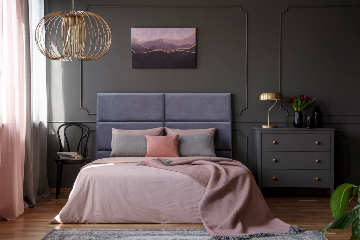 An elegant apartment interior for a woman with grey chest of drawers standing next to a pink bed with a grey cushioned headboard