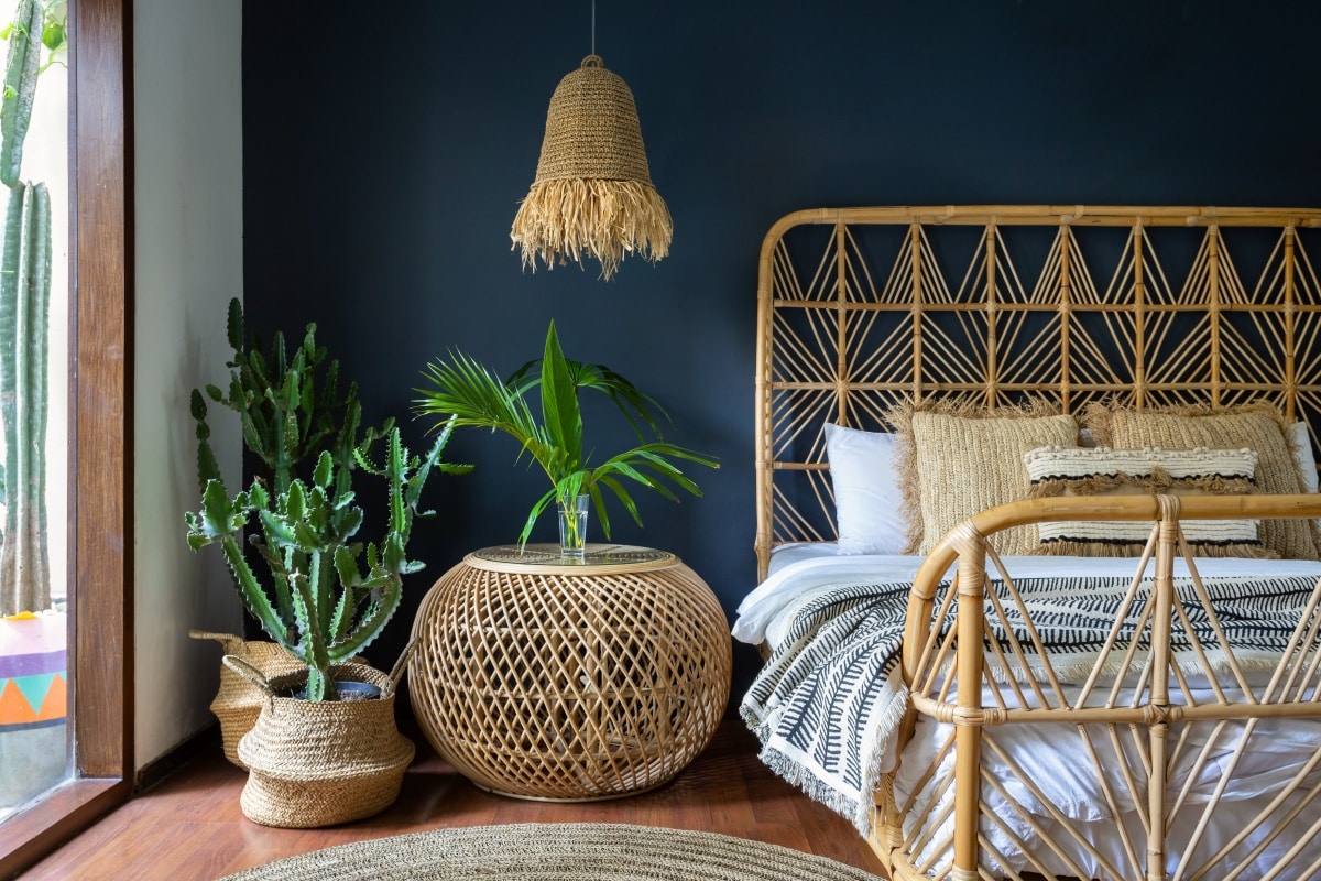 Traditional Asian bedroom with ethnic decor, lamp over nightstand table, comfortable bed, carpet or rug, exotic cactus in basket and natural green plant