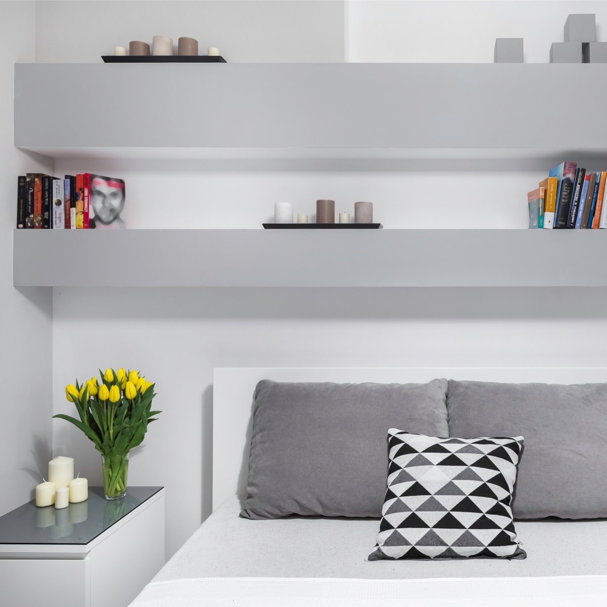 White floating shelves above bed with white sheets and grey pillows