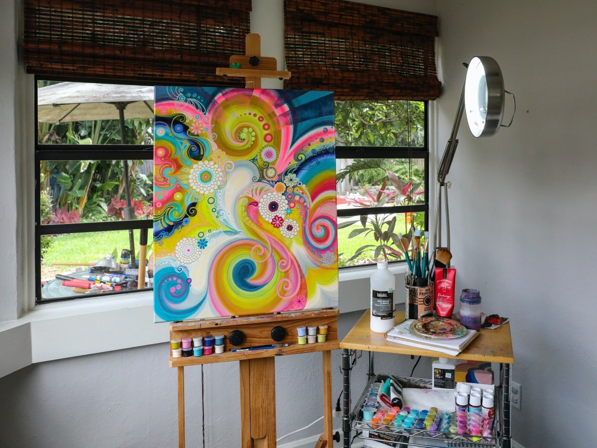A colourful painting and art supplies in a room overlooking a garden