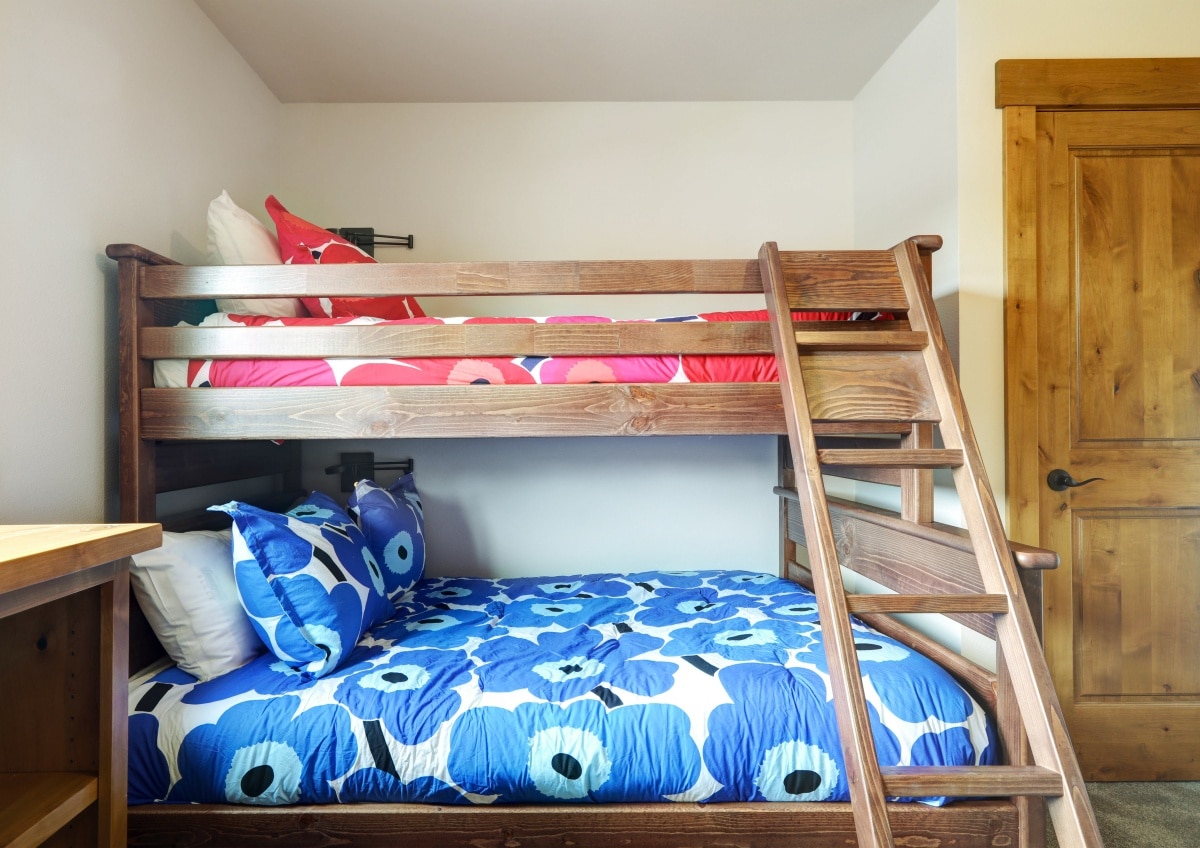 A bunk bed in blue and red bedding with large flowers print and grey carpet.