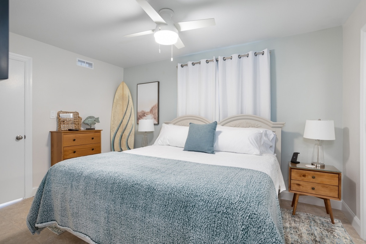 simple bedroom with cozy bed and a surfboard in a corner