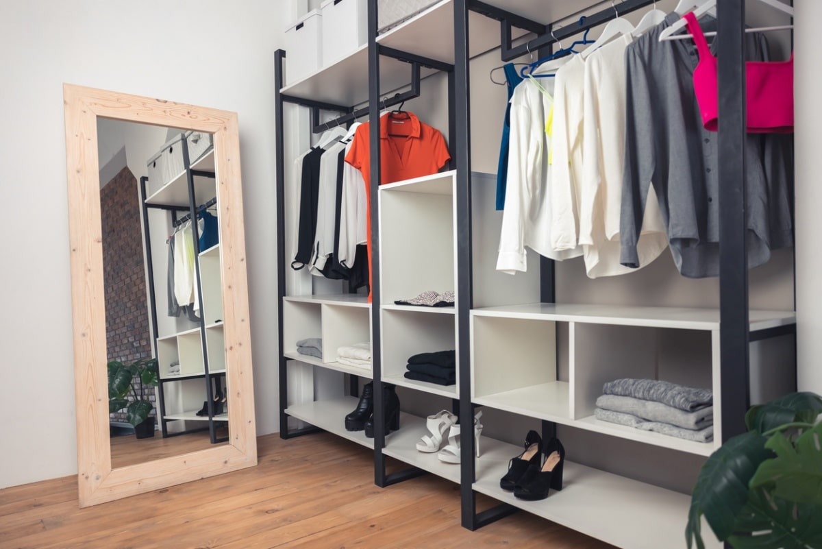 garmet closet with trendy clothes on metal racks and a full-length mirror propped against a wall