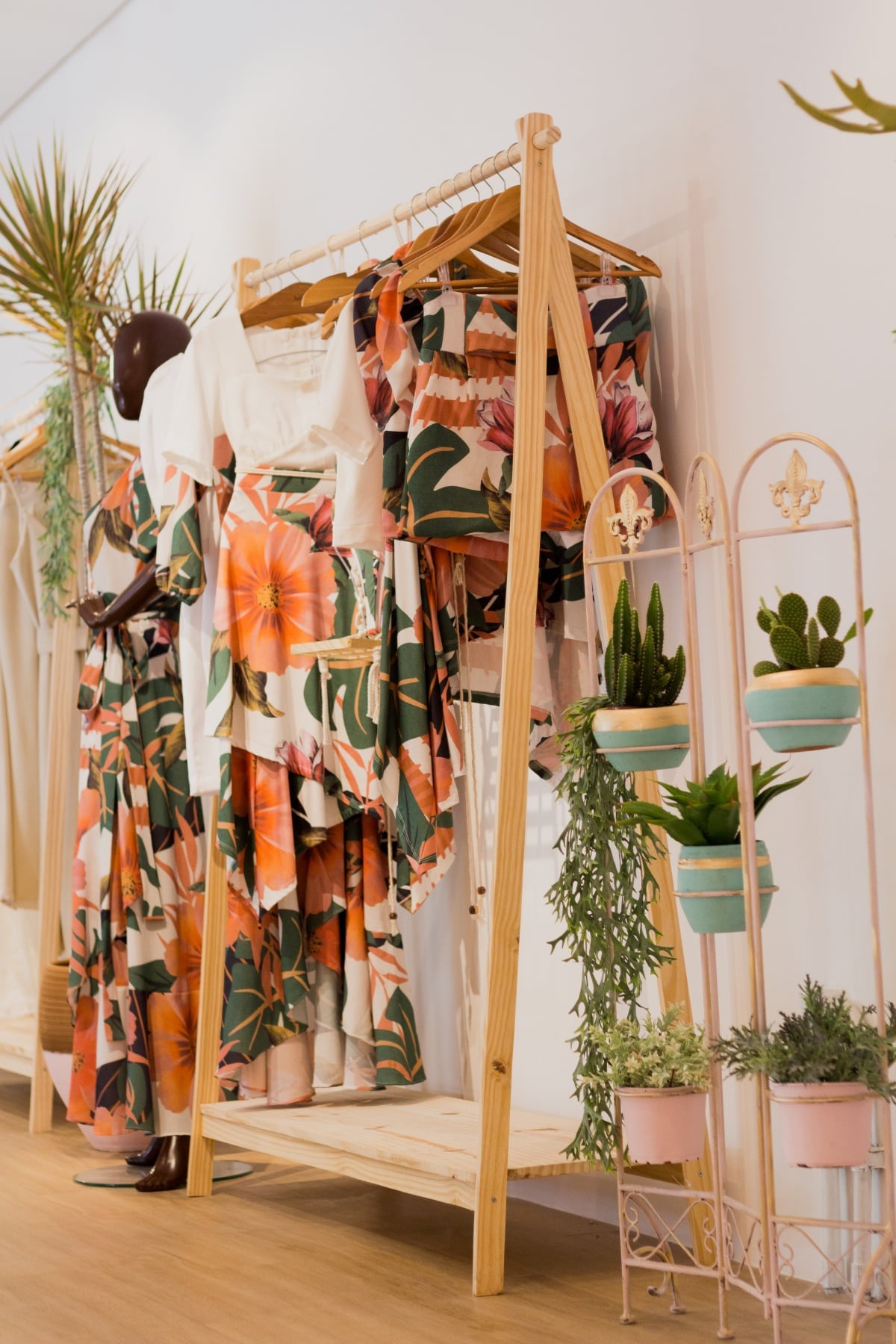 Tropical printed clothes on a rack in a room with plants and plain white wall