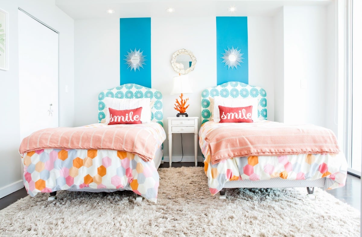 Two beds with matching patterned quilts, patterned headboards, and red pillows in a modern bedroom