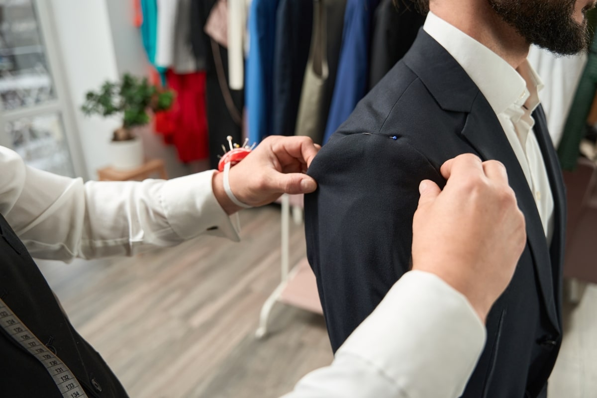 A tailor applying alterations to a groom's suit.