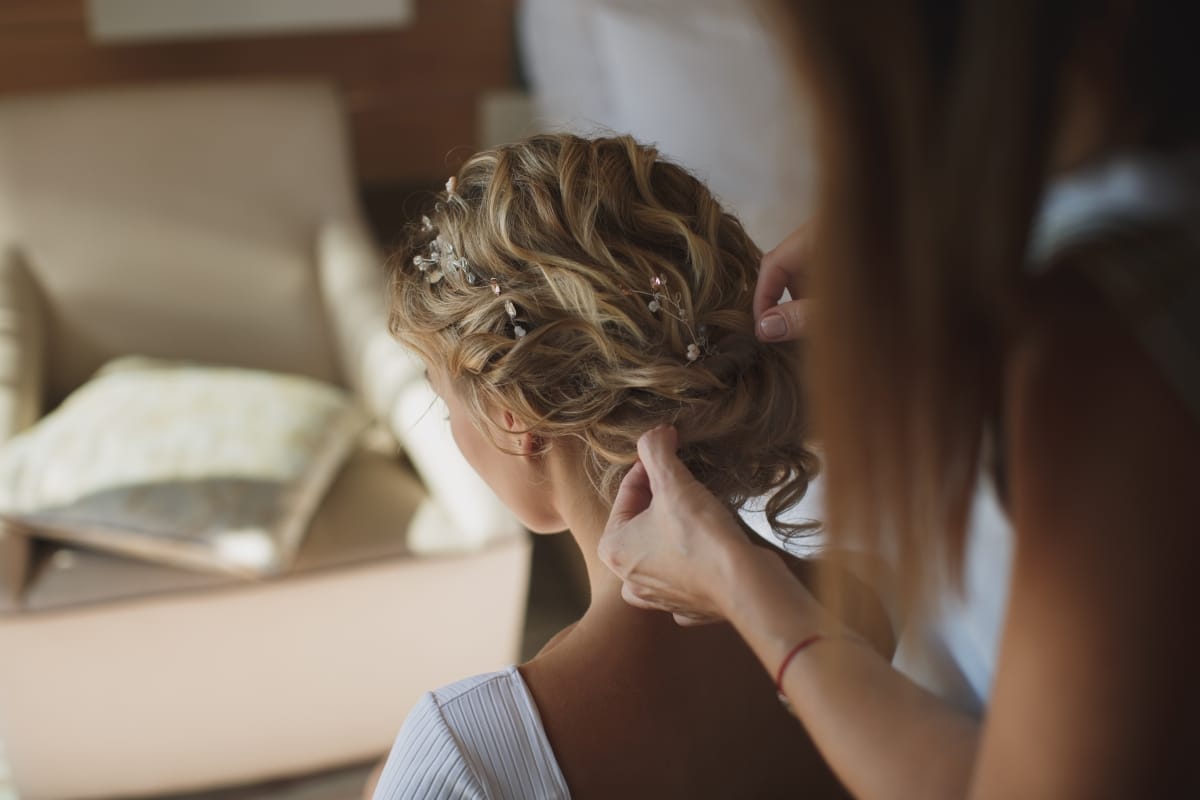 A professional hairstylist arranging the bride's hair for her wedding day.