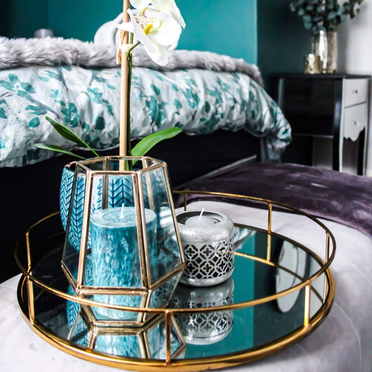 a gold tray with a teal candle and vase