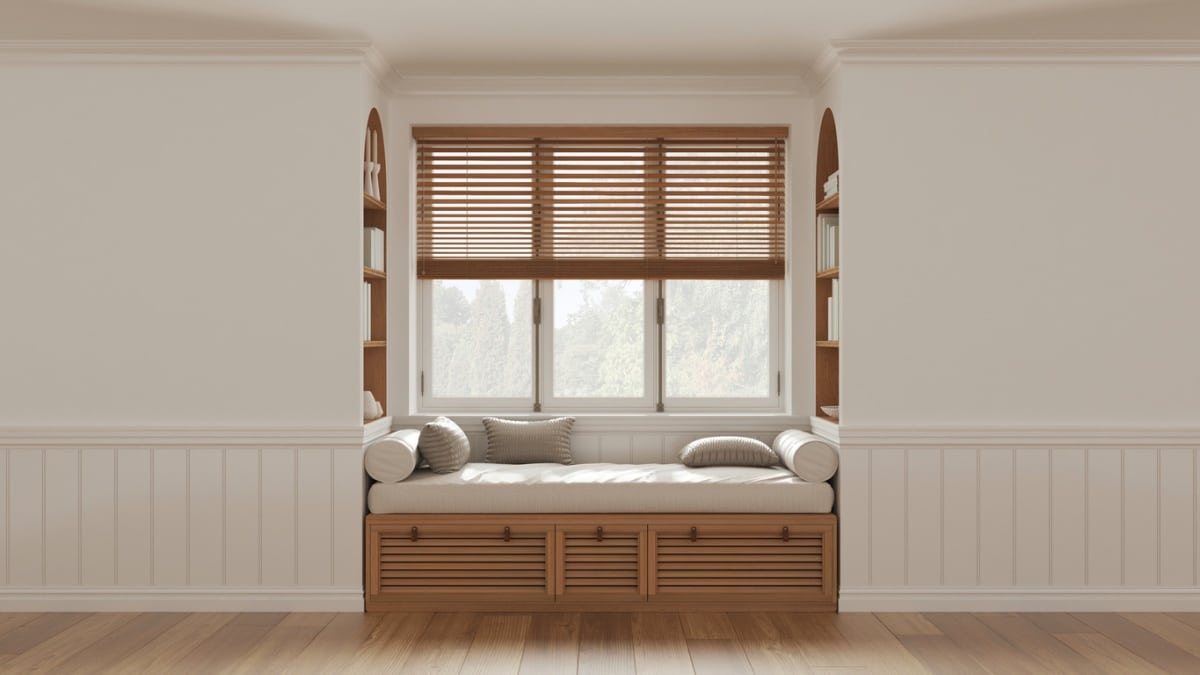 Classic window with sitting bench and pillows, wooden venetian blinds, bookshelf, and decor