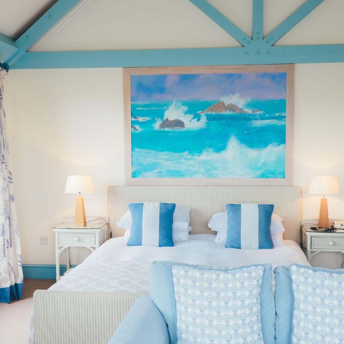 a white and blue bedroom with lamps on nightstands and a painting hanging over the bed