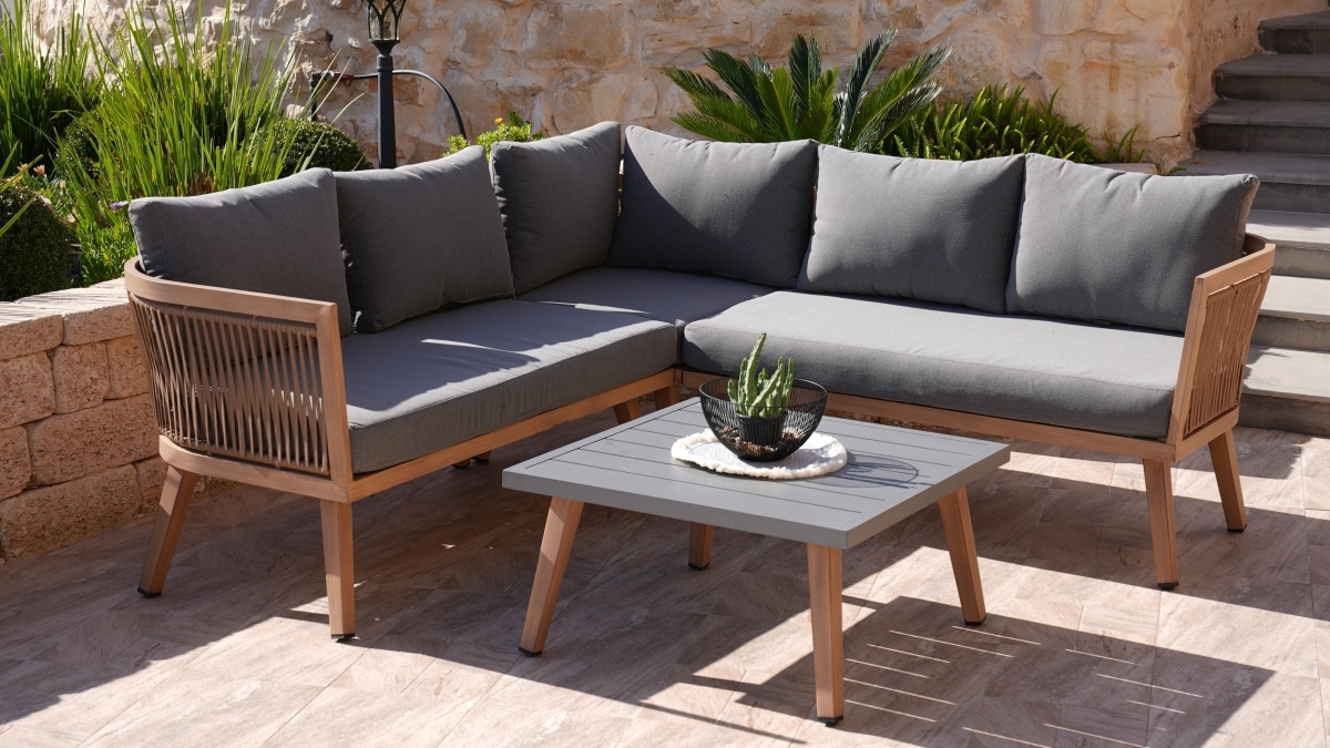 A wooden corner sofa with gray pillows and table in garden