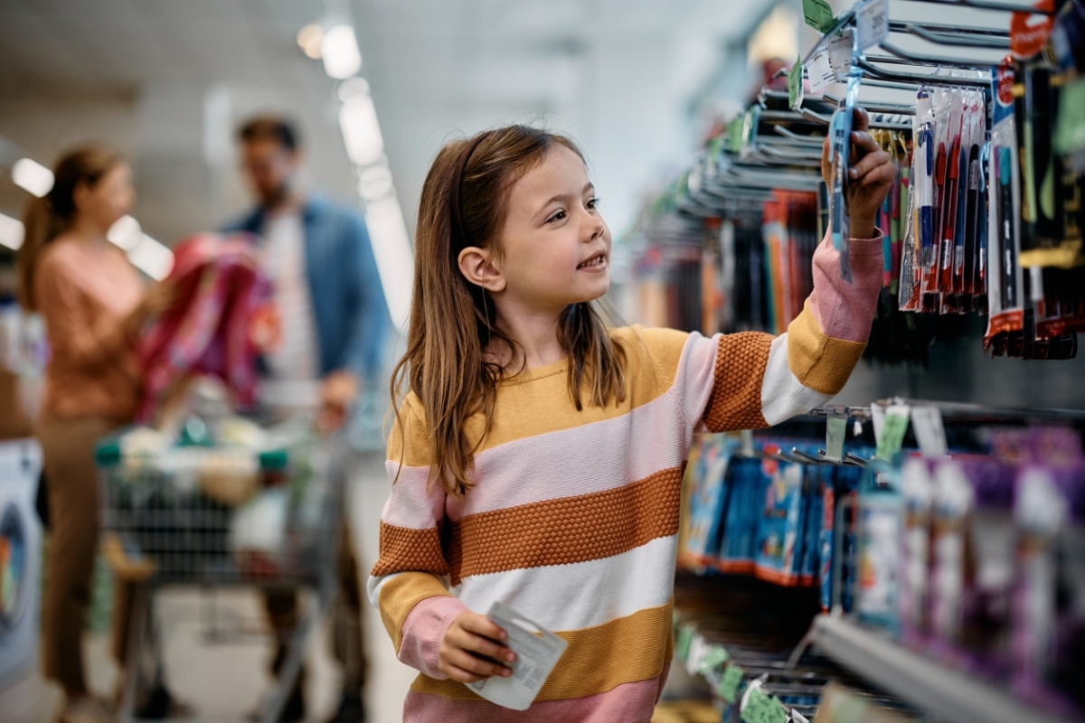 Smiling little girl choosing school supplies while being with her parents in a bookstore.