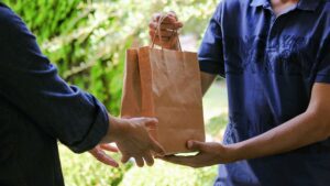 Young delivery man standing at the door of the house and carrying food to be delivered